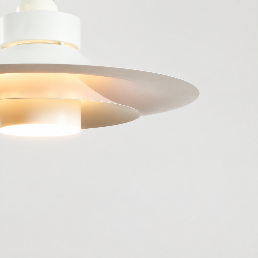 A close-up of a modern white pendant light fixture with layered circular shades, shown illuminated against a clean white background.