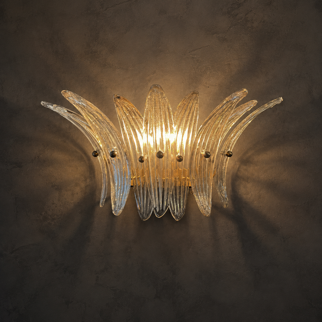 A curved, multi-light wall sconce made of ribbed clear glass, glowing with a warm yellow light against a dark textured wall.