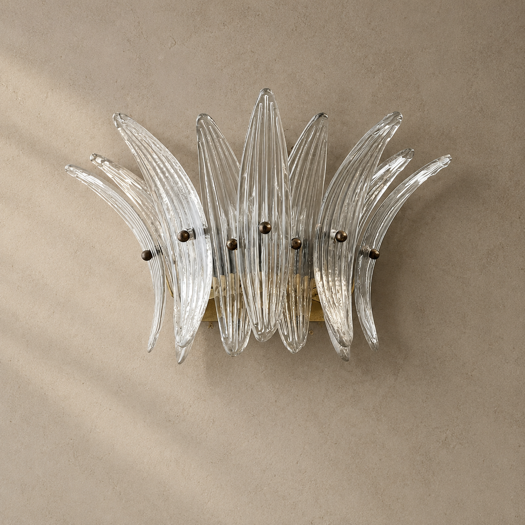 Wall sconce with clear ribbed glass leaves and a gold-toned frame mounted on a textured beige wall.