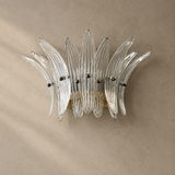 Wall sconce with clear ribbed glass leaves and a gold-toned frame mounted on a textured beige wall.