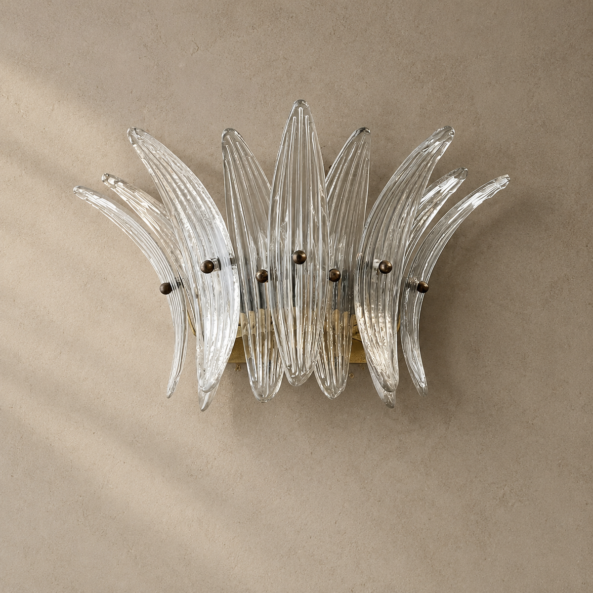 Wall sconce with clear ribbed glass leaves and a gold-toned frame mounted on a textured beige wall.