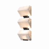 A modern three-light wall sconce featuring textured, translucent white stone or acrylic geometric blocks mounted on a slim black metal frame, shown against a solid white background.