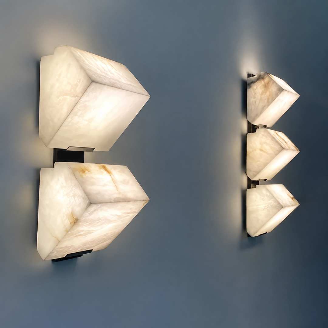 Two-light and three-light alabaster wall sconce designs with black frames glow against a blue wall.