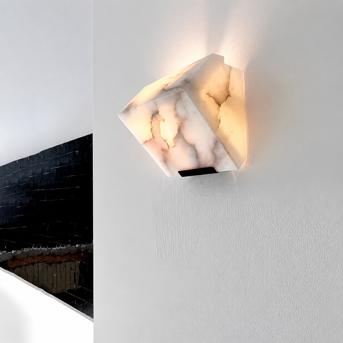 A modern geometric wall sconce made of white marble with warm yellow lighting glowing from within, mounted on a textured white wall.