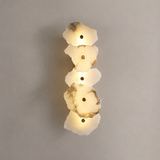 A vertical wall sconce featuring four stacked, irregular polished stone slices glowing with warm light against a neutral gray wall.