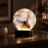 A glowing white agate crystal sphere lamp on a dark metallic base, sitting on a wooden table in a dimly lit living room.