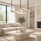 Cream alabaster double-ring chandelier hangs from brown leather straps above a stone coffee table in a bright living room.