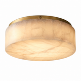 A flush-mount ceiling light fixture with a warm, glowing oval shade made of textured cream-colored stone or acrylic, framed by a brushed brass metal rim at the top.