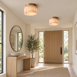 Two illuminated alabaster drum flush mount lights with gold-toned ceiling plates brighten an entryway with a wooden door and console.