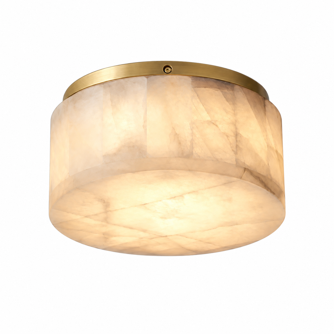 A modern flush-mount ceiling light fixture featuring a warm, glowing oval shade made of textured cream and beige stone, with a polished gold brass top canopy.