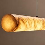 Close-up of a linear pendant light with a glowing marble cylinder and dark suspension cable against a taupe background.