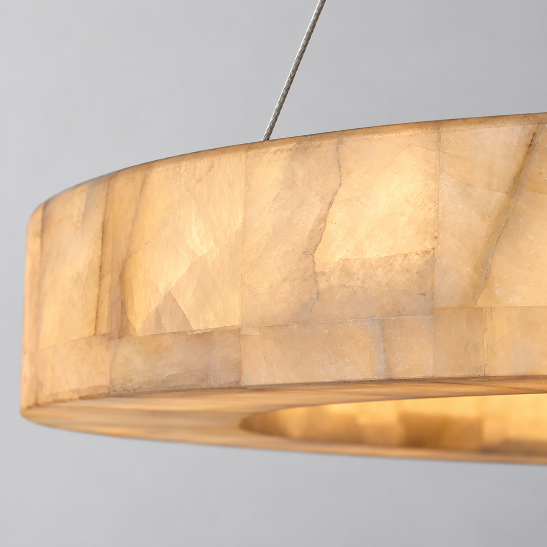 Close-up of the ring chandelier shows glowing cream alabaster panels, natural veining, and a suspension cable against a grey background.
