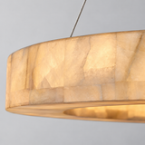 Close-up of the ring chandelier shows glowing cream alabaster panels, natural veining, and a suspension cable against a grey background.