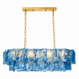 Linear chandelier with layered blue glass panels and gold-toned chains is shown illuminated against a white background.