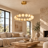 An illuminated alabaster ring chandelier hangs above a wooden coffee table beside a beige sofa and stone fireplace.