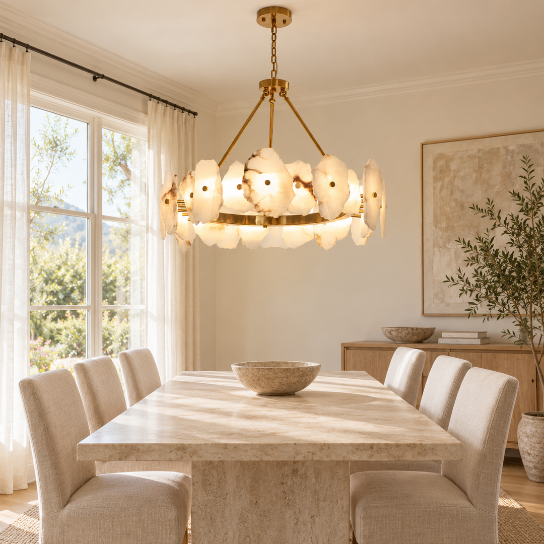 A modern chandelier with glowing white petal-shaped glass shades hangs over a light stone dining table and upholstered chairs in a bright, sunlit dining room.