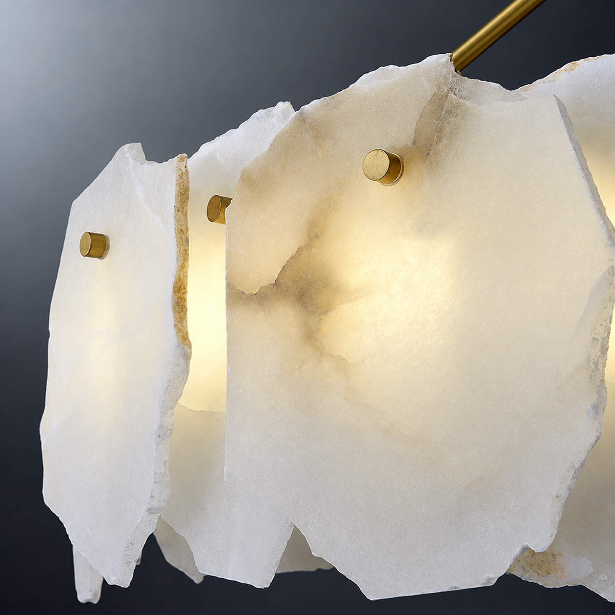 Close-up of a chandelier with illuminated, irregular-edged white alabaster panels and gold-tone fasteners against a dark gray background.