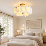 A modern semi-flush mount ceiling light with a warm glowing organic shell-like shade and a gold brass top canopy, installed in a bright, neutral-toned bedroom.