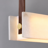 Close-up of a glowing white alabaster linear pendant light with a brown leather strap and round gold-tone fastener against a gray background.