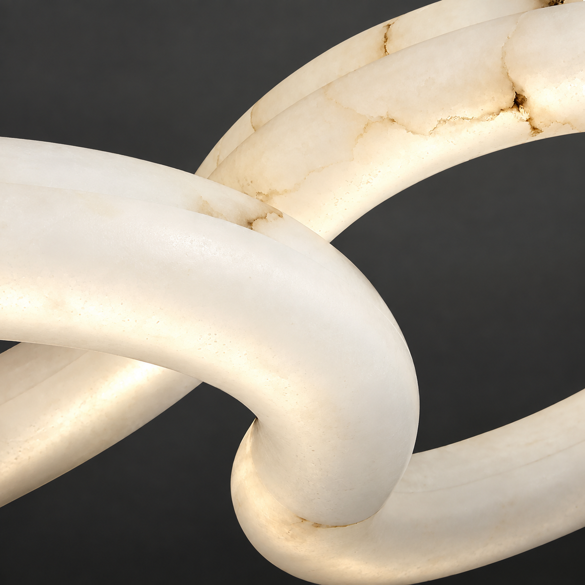 Close-up of the chandelier’s illuminated cream alabaster rings shows brown veining and overlapping curves against a dark background.