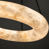 Close-up of an illuminated alabaster ring chandelier showing cream and tan veining against a dark background.