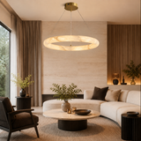 Glowing alabaster ring chandelier with a brass canopy above a round coffee table in a living room with a cream sectional.