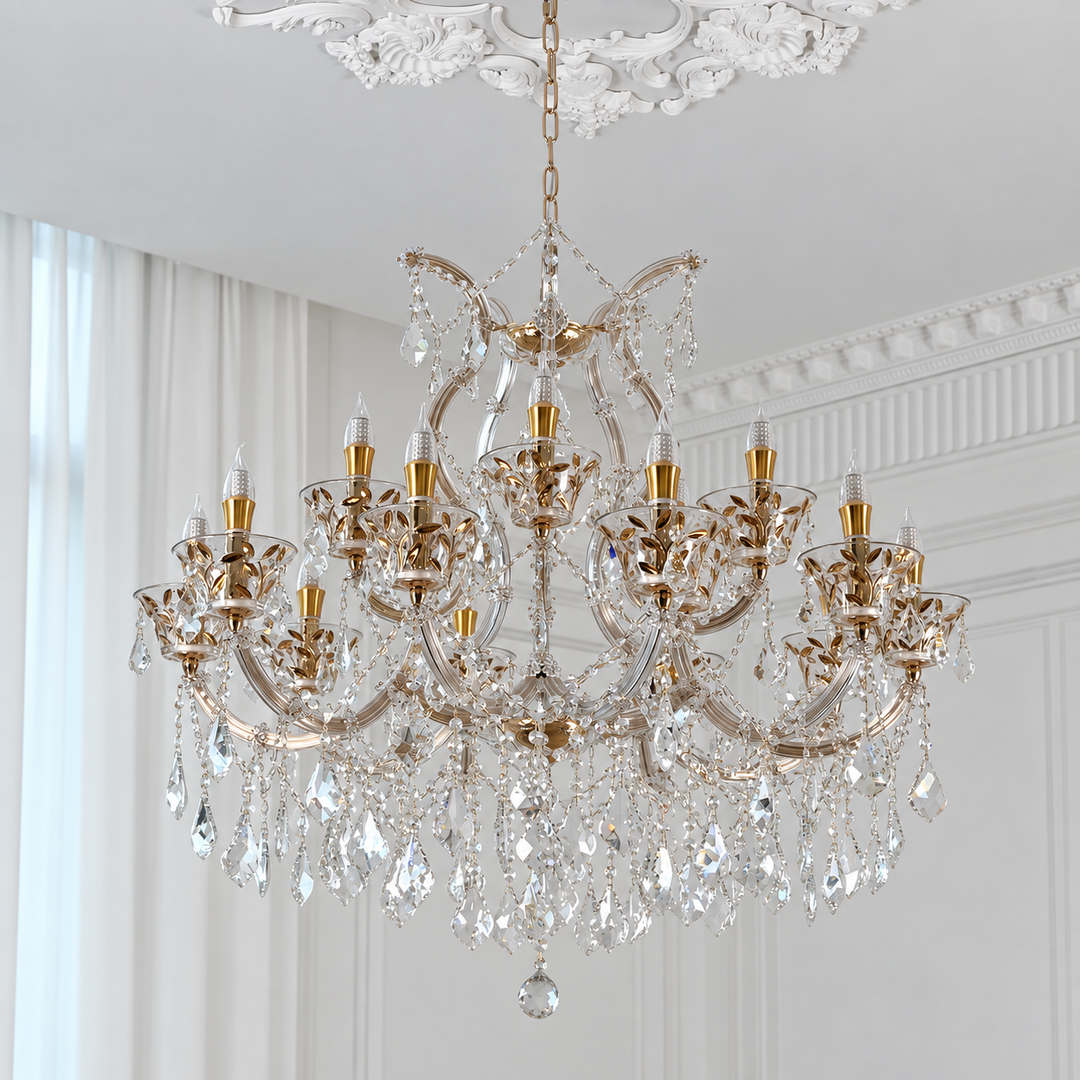 An ornate multi-light crystal chandelier with gold-toned metal arms and hanging clear glass prisms, suspended from a decorative ceiling in a bright white room.