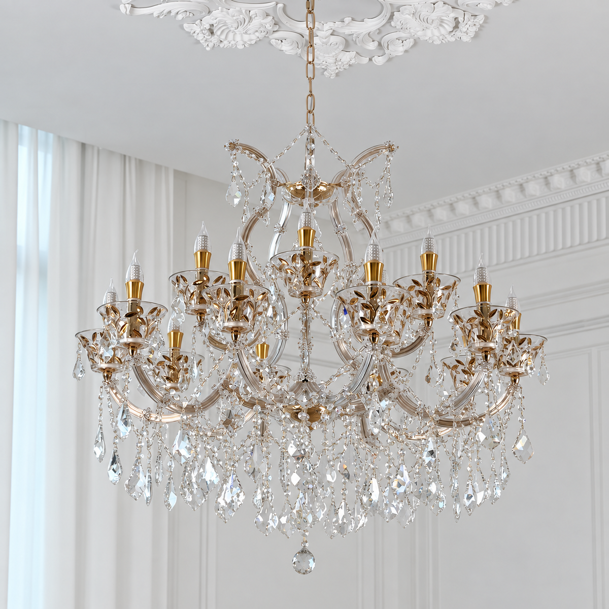 An ornate multi-light crystal chandelier with gold-toned metal arms and hanging clear glass prisms, suspended from a decorative ceiling in a bright white room.