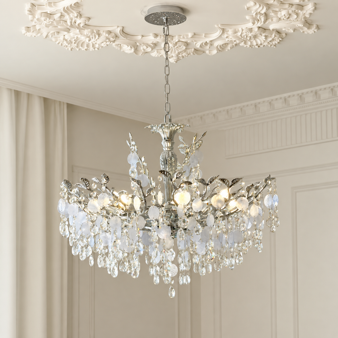 A multi-tiered crystal chandelier with a silver-toned metal frame, hanging from a decorative ceiling canopy in an elegant room with cream walls and molding.