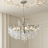 A multi-tiered crystal chandelier with a silver-toned metal frame, hanging from a decorative ceiling canopy in an elegant room with cream walls and molding.