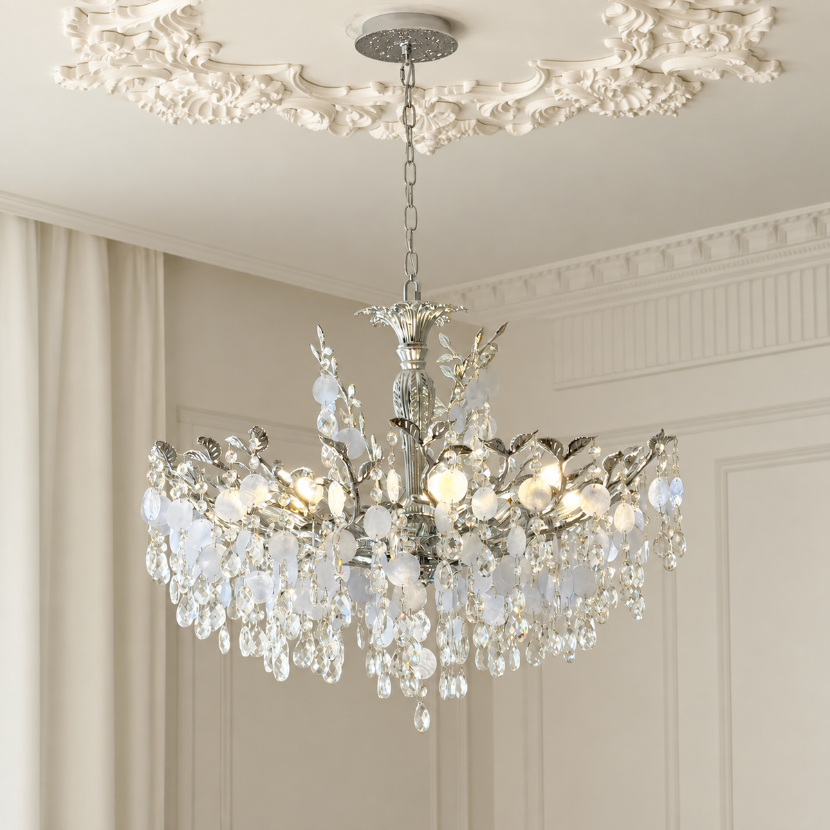 A multi-tiered crystal chandelier with a silver-toned metal frame, hanging from a decorative ceiling canopy in an elegant room with cream walls and molding.