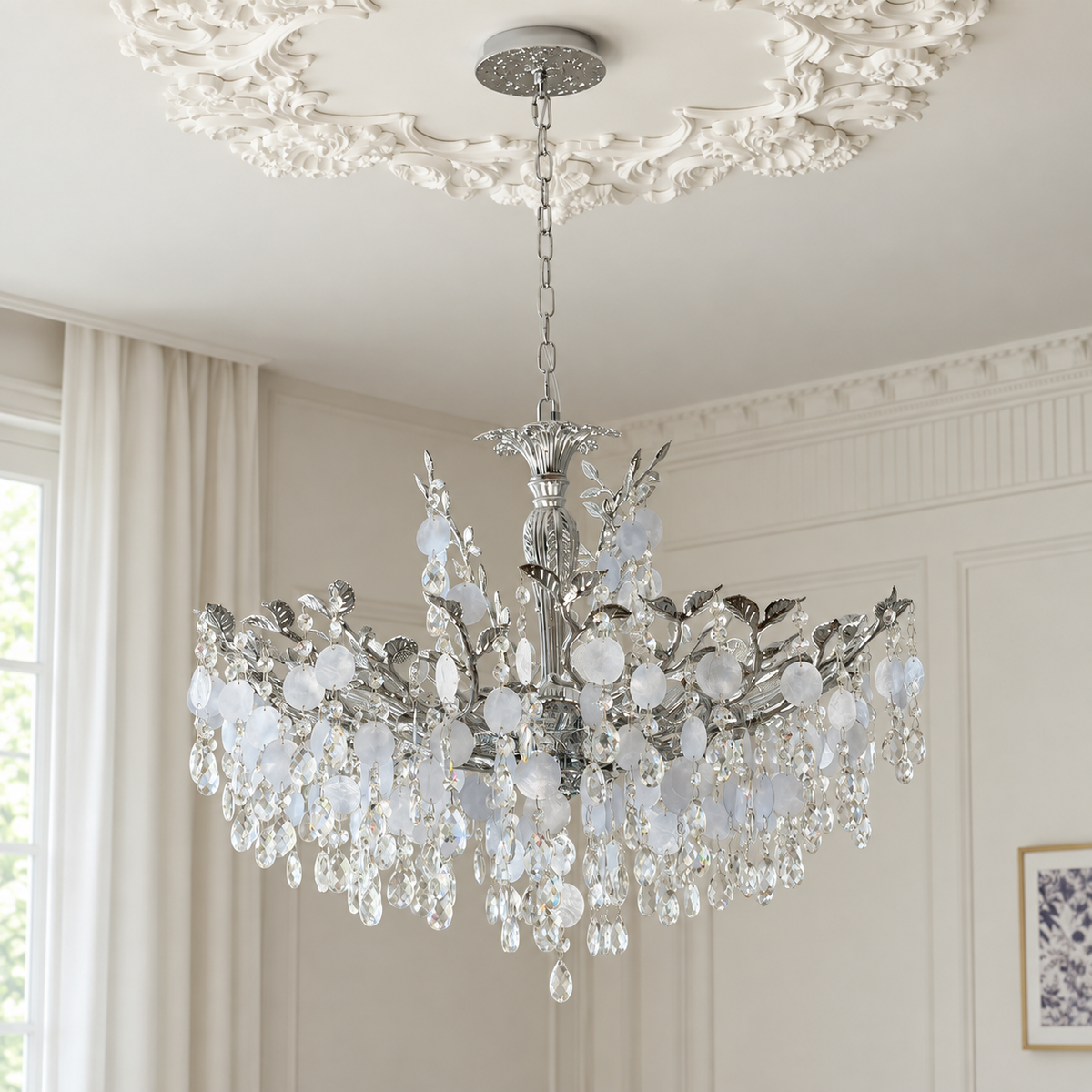 A silver-toned crystal chandelier with clear and frosted glass droplets, hanging from an ornate white ceiling medallion in a bright, classic room with cream walls and curtains.
