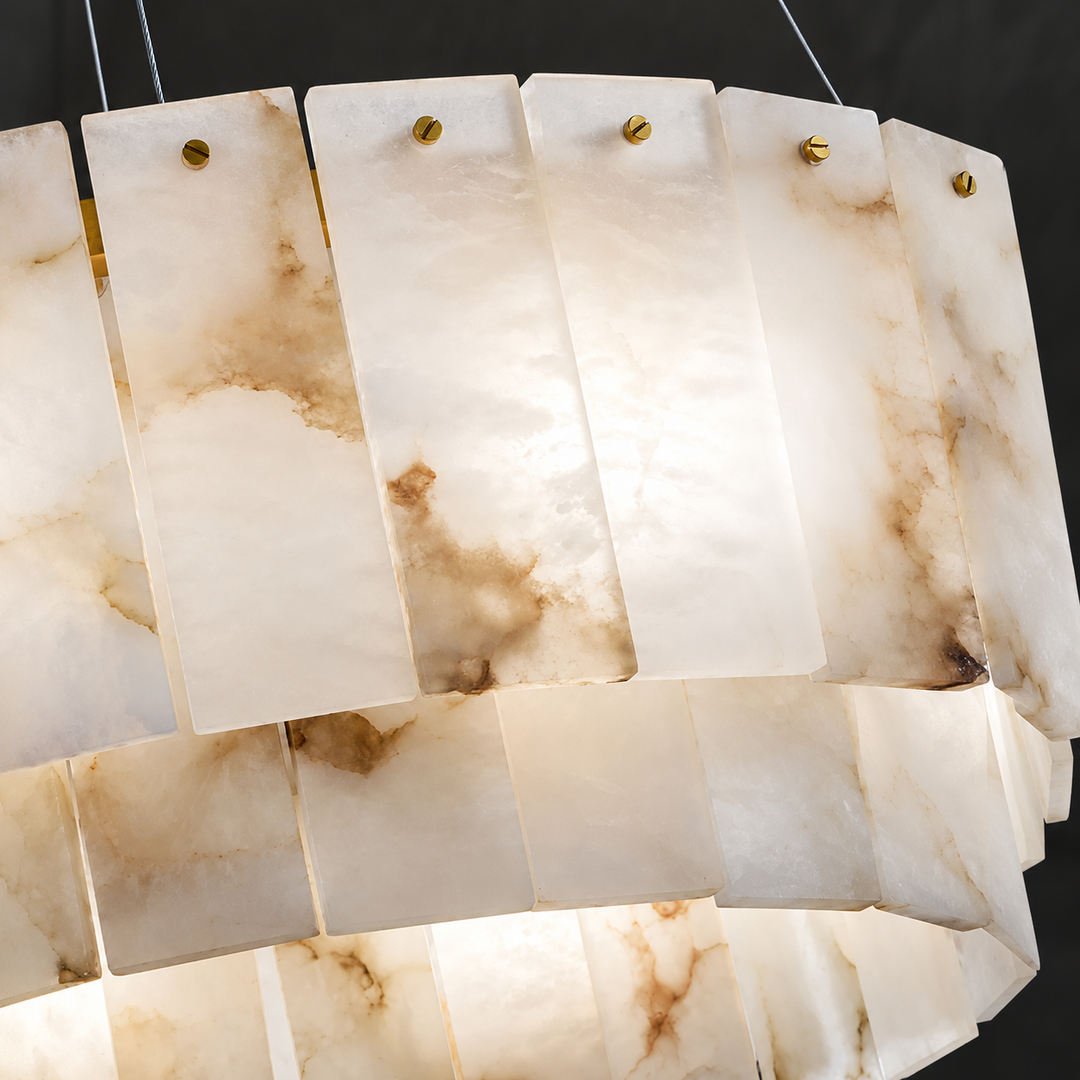 A close-up of a modern chandelier featuring rectangular translucent stone panels with natural beige and brown marbling, suspended by thin wires with gold-toned hardware.