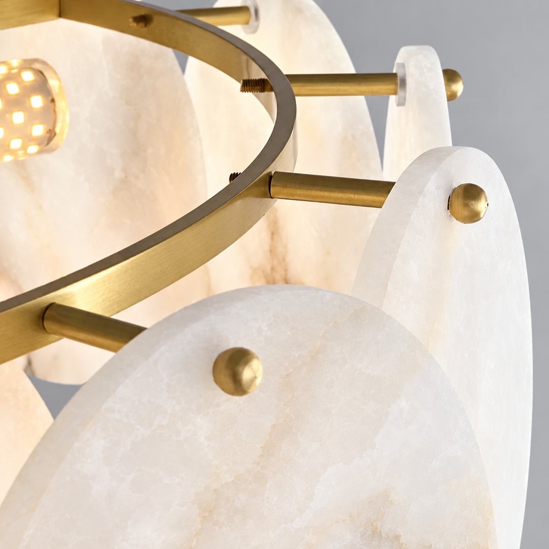 Close-up of a modern chandelier featuring oval white alabaster stone shades and brushed gold metal hardware, with a warm glowing light bulb visible.