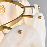 Close-up of a modern chandelier featuring oval white alabaster stone shades and brushed gold metal hardware, with a warm glowing light bulb visible.