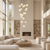 A modern multi-light pendant chandelier with numerous spherical glass globes hangs in a tall, bright contemporary living room with a fireplace, built-in shelves, and light beige furniture.