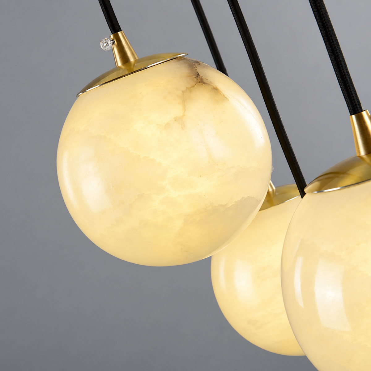 Close-up of a chandelier with glowing cream alabaster globes, gold-toned caps, and black suspension rods against a gray background.