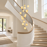A modern multi-light chandelier with hanging spherical glass globes is displayed in a bright, contemporary spiral staircase lobby with light wood steps and white walls.