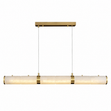A modern linear pendant light fixture with a horizontal bar of textured, warm off-white glass shades and polished brass hardware, suspended by two thin cables from a matching brass ceiling canopy.