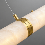 Close-up of a linear pendant with glowing cream alabaster, gold-toned detailing and a suspension cable against a grey background.