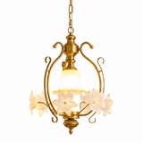 Gold-tone pendant light with a warm glowing bell shade and cream frosted glass flowers, against a white background.