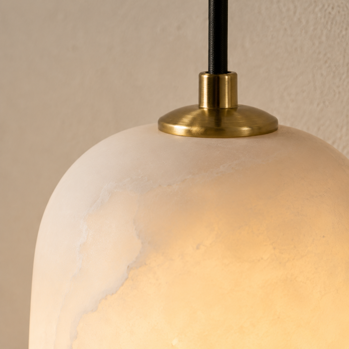 A close-up of the wall sconce shows its glowing, veined alabaster shade, brass top cap, and black suspension against a beige wall.