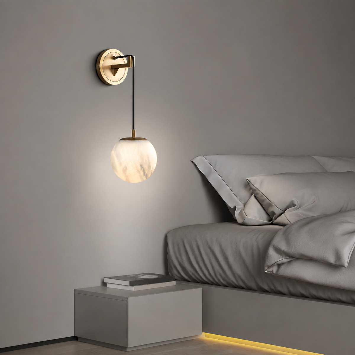 Wall pendant with a glowing alabaster globe, black cord and brass mount beside a gray bed above a low bedside table.