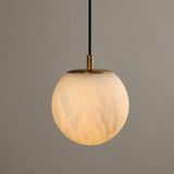 Wall pendant close-up showing a glowing, veined alabaster globe with a brass cap and black cord against a gray background.