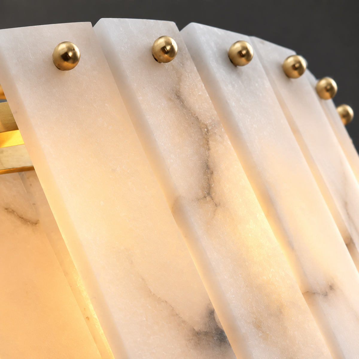 Close-up of the chandelier’s white alabaster panels with gray veining and round gold-tone fasteners, glowing warmly against a dark background.
