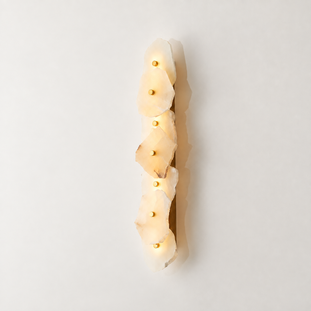 A vertical wall sconce featuring five stacked, irregular natural stone slices that glow warm white when lit, with small gold-toned bulbs set into the center of each stone. The fixture is shown against a clean, off-white background with a soft shadow.