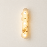 Alabaster wall sconce shown at an angle on a pale wall, with overlapping cream stone petals, brass-tone accents, and warm illumination.