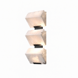 A modern three-light wall sconce featuring textured white stone or marble cube shades with black metal brackets, shown against a plain white background.