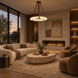 A modern living room interior with a large cream sectional sofa, two rounded brown accent chairs, a round stone coffee table, a lit linear fireplace on a textured wall, and a circular pendant chandelier overhead.