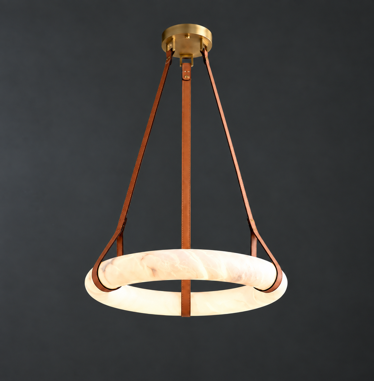 Chandelier with a glowing cream alabaster ring suspended from brown leather straps beneath a brass canopy against dark gray.